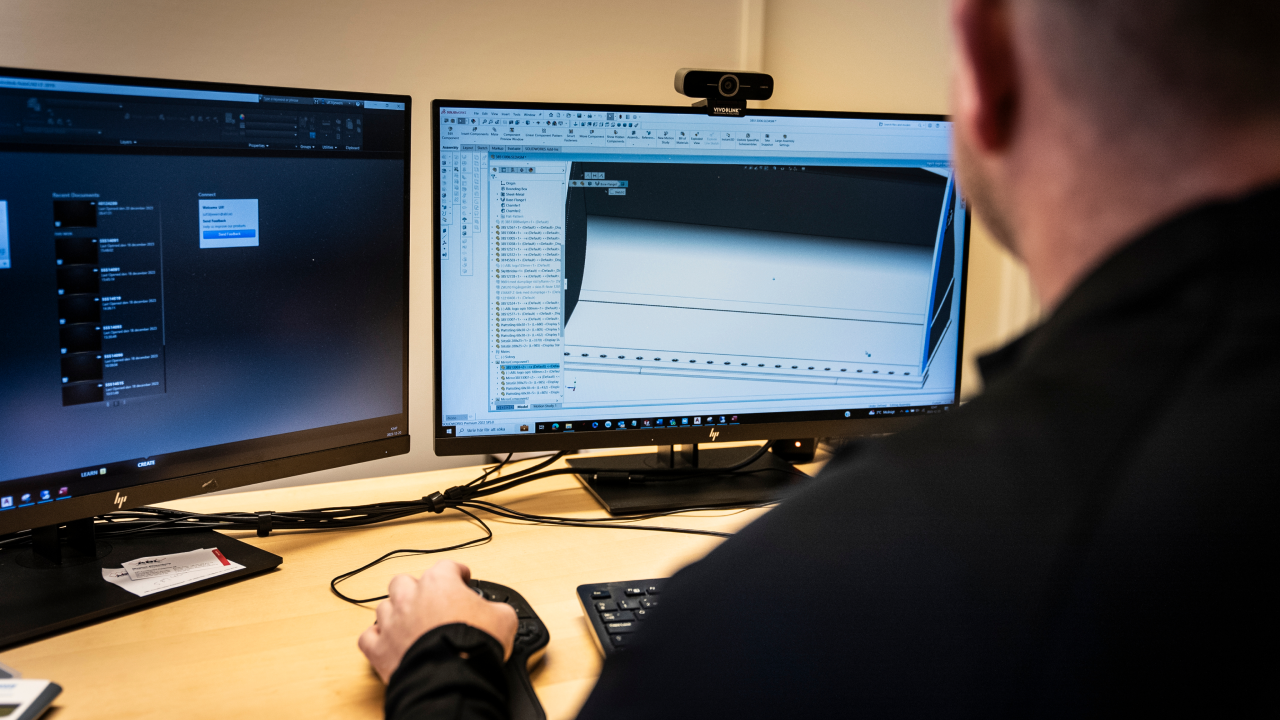 ABL’s design engineer sitting in front of two computer screens showing CAD models of a bucket.