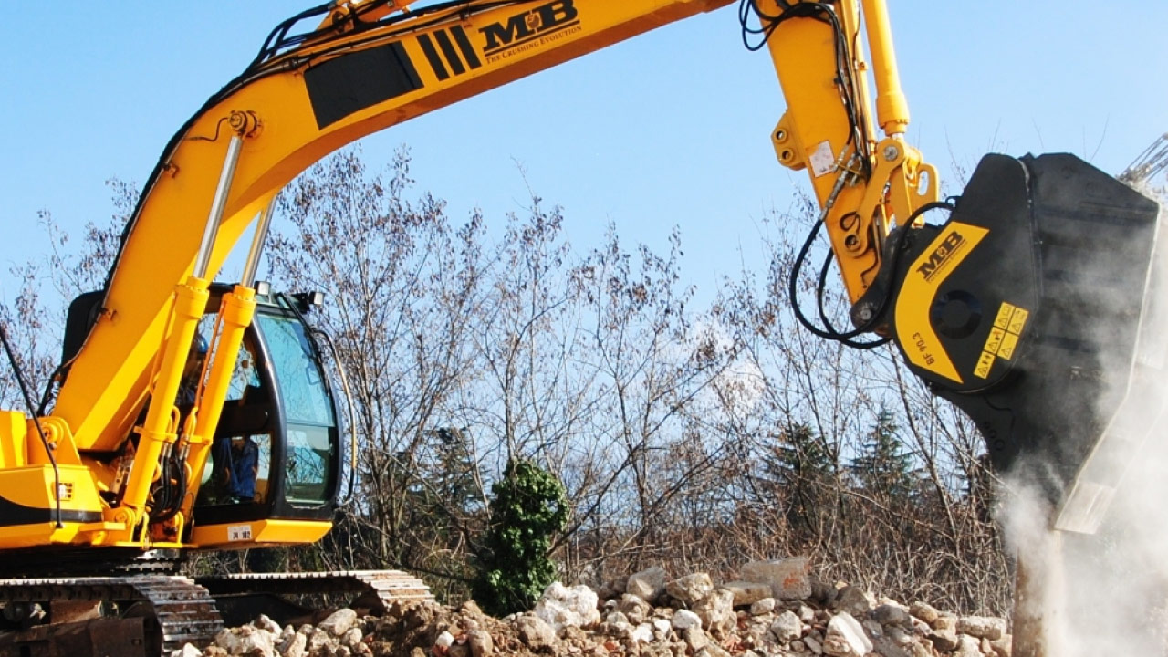 A yellow tracked excavator dumping abrasive rocks, with excavator bucket made in Hardox 400 wear steel.